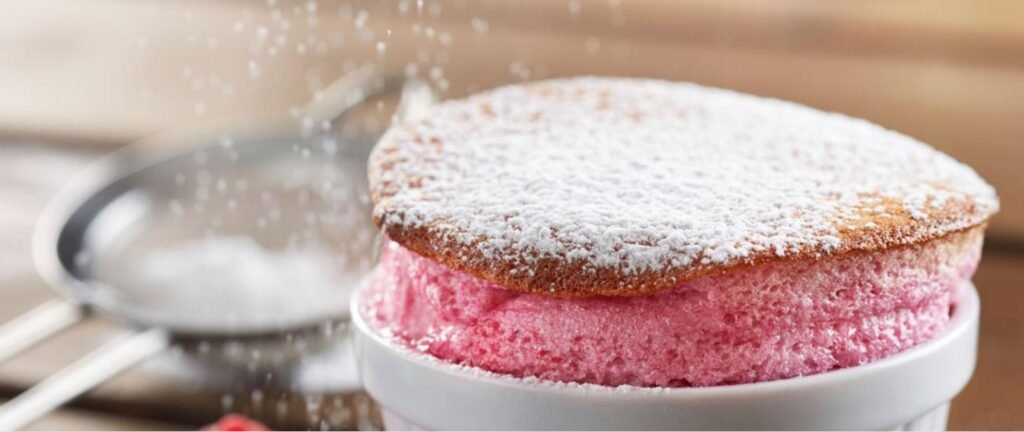 Light and airy raspberry soufflé in a white ramekin, topped with powdered sugar and fresh raspberries